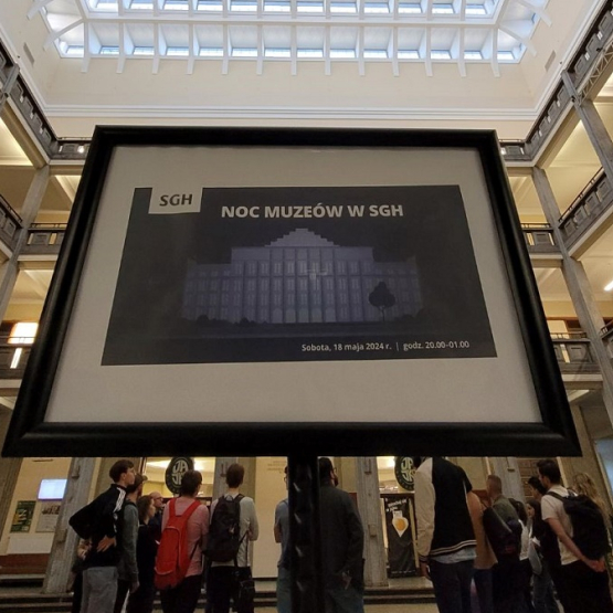 grupa osób zwiedza budynek; na pierwszym planie tablica z napisem "Noc Muzeów SGH"