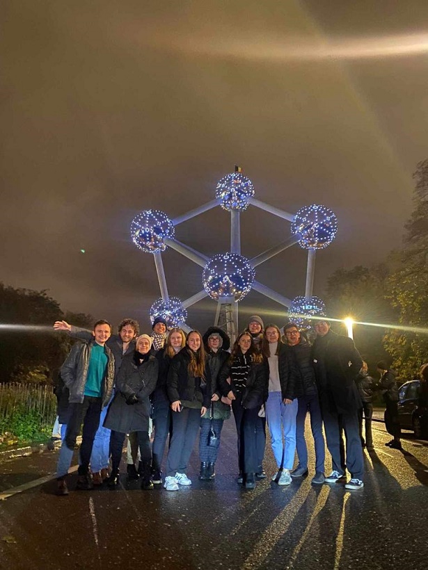 grupa osób w porze wieczornej pozuje do zjęcia na tle modelu atomu w Brukseli