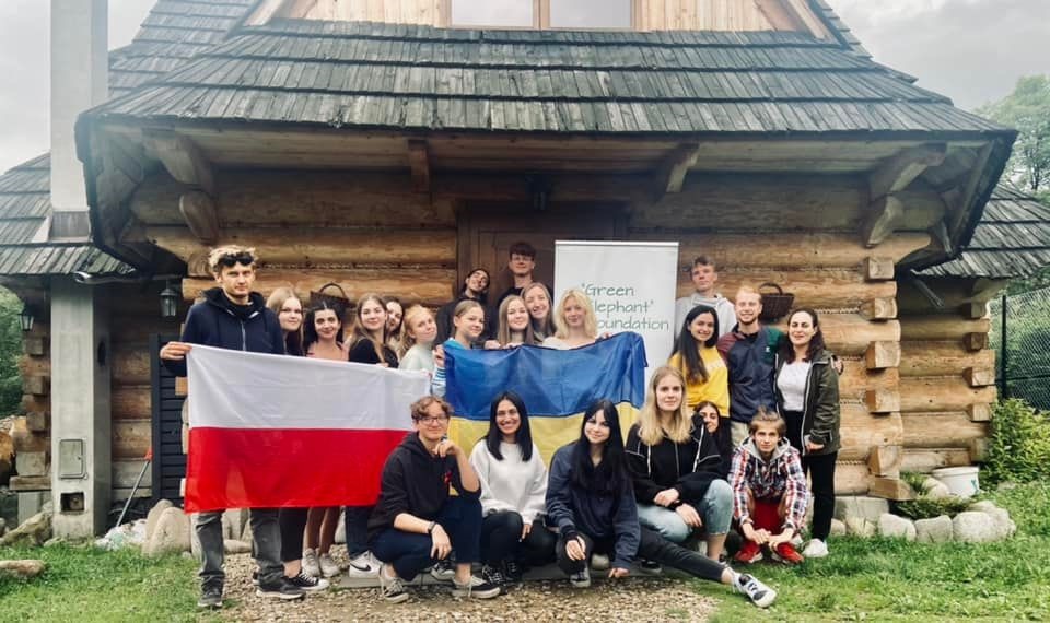 grupa młodych osób stoi przed chatą góralską, część z nich trzyma flagi Polski i Ukrainy