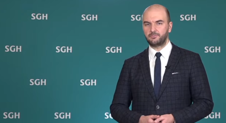 Dr hab. Krzysztof Kozłowski, prof. SGH, prorektor ds. dydaktyki i studentów na tle zielonej ścianki z logo SGH