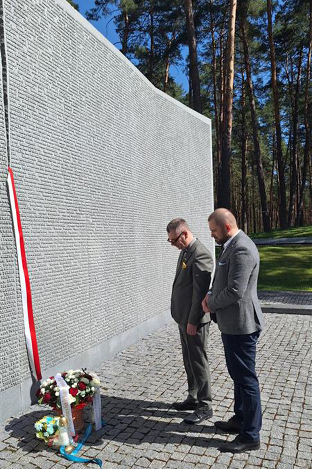 Rektor Piotr Wachowiak i kanclerz Marcin Dąbrowski składają kwiaty przy pomniku ofiar zbrodni katyńskiej w Bykowni