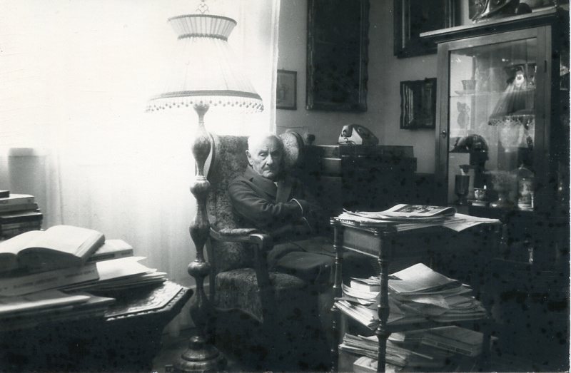 mężczyzna siedzący w fotelu w swoim gabinecie, zawalonym książkami