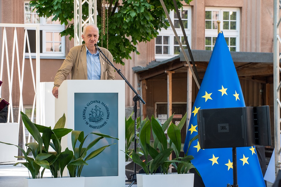 męzczyzna przemawiający za pulpitem; z przodu sceny flaga UE