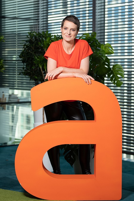 uśmiechnięta kobieta oparta o plastikowy pomarańczowy napis reklamowy firmy Allegro