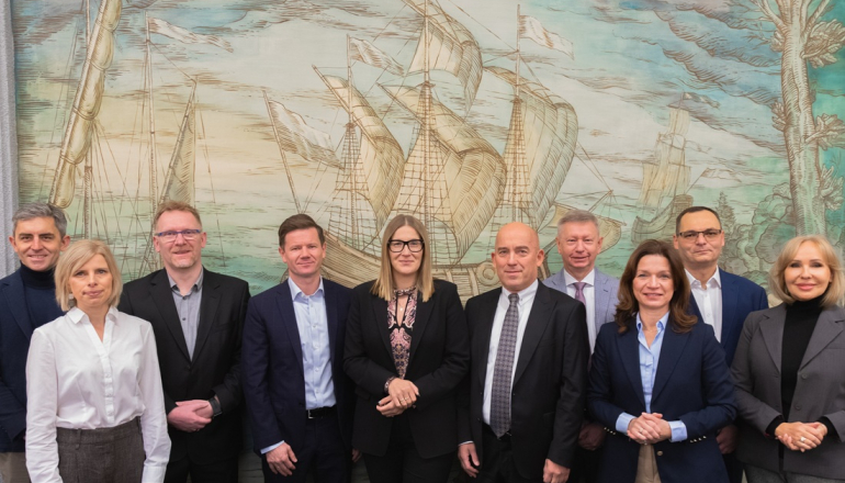 grupa osób pozuje do zdjęcia na tle fresku statku handlowego