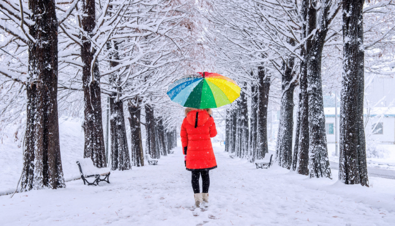 człowiek idący w śnieżnej alei z kolorowym parasolem