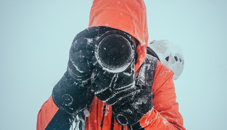 mężczyzna w czerwonej kurtce z aparatem fotograficznym
