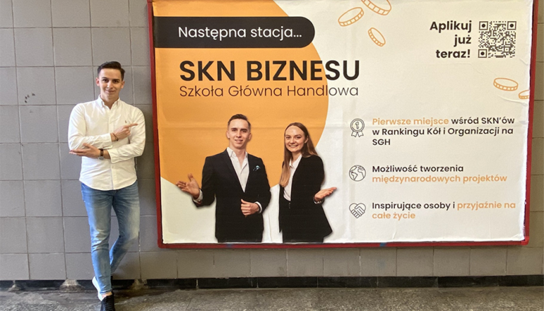 na zdjęciu mężczyzna wskazujący bilbord na ścianie z napisem SKN Biznesu Szkoła Główna Handlowa