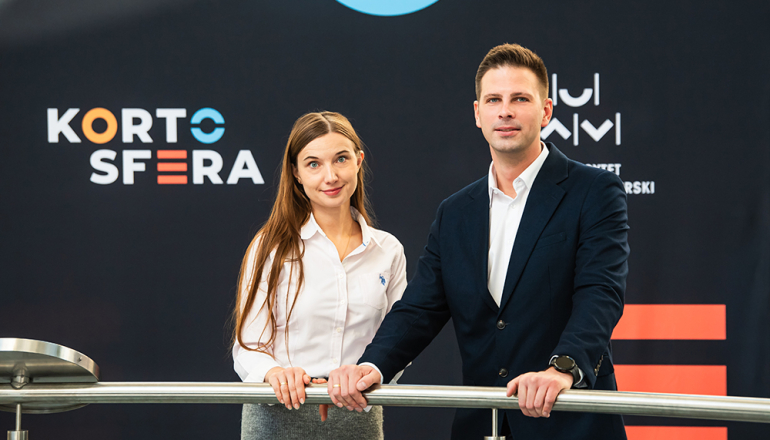 Kobieta i mężczyzna przy barierce na tle banera z napisem Kortosfera