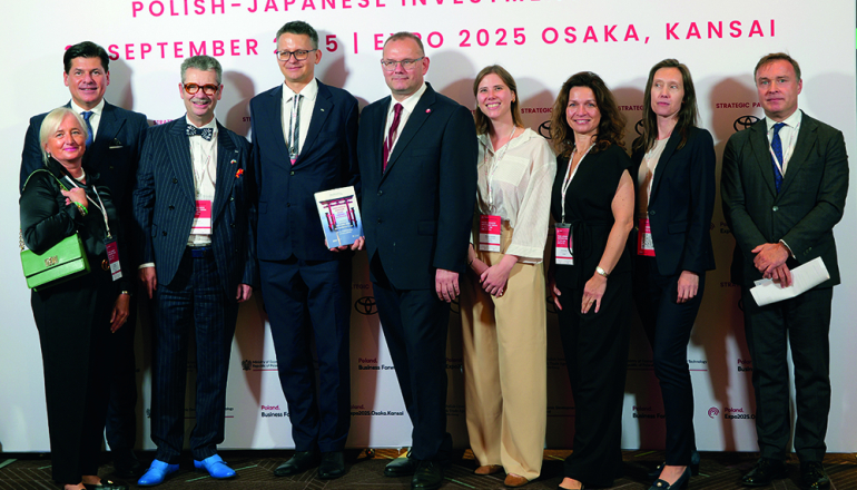 Dziewięć osób w oficjalnych strojach na tle baneru polsko-japońskiego forum inwestycyjnego