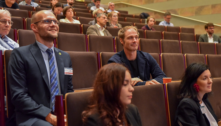 ludzie siedzący w ławkach w auli I budynku C