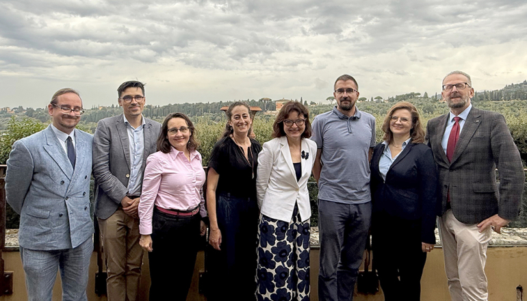 Osiem uśmiechających się osób, stojących na tle toskańskiego krajobrazu 