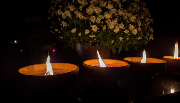 trzy ceramiczne znicze płonące na nagrobku stojące obok kwiecistej chryzantemy