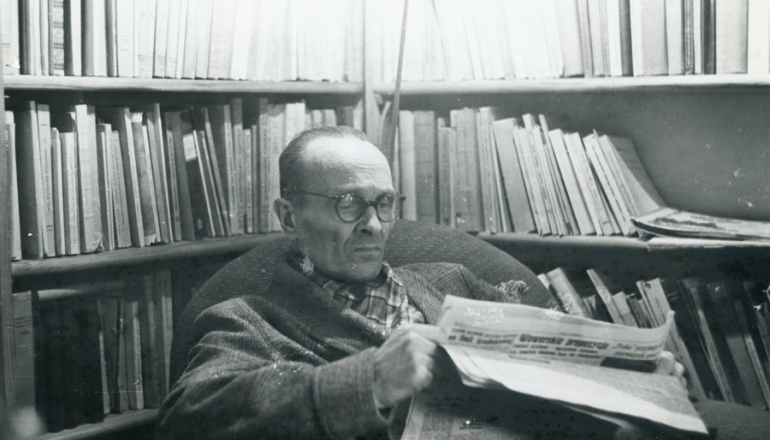 czarno-białe zdjęcie mężczyzny siedzącego w gabinecie pełnym książek i czytającego gazetę