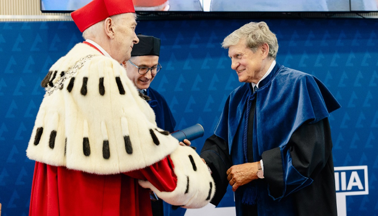 dwóch mężczyzn w togach; jeden w todze rektorskiej składa gratulacje drugiemu w todze doktora honoris causa