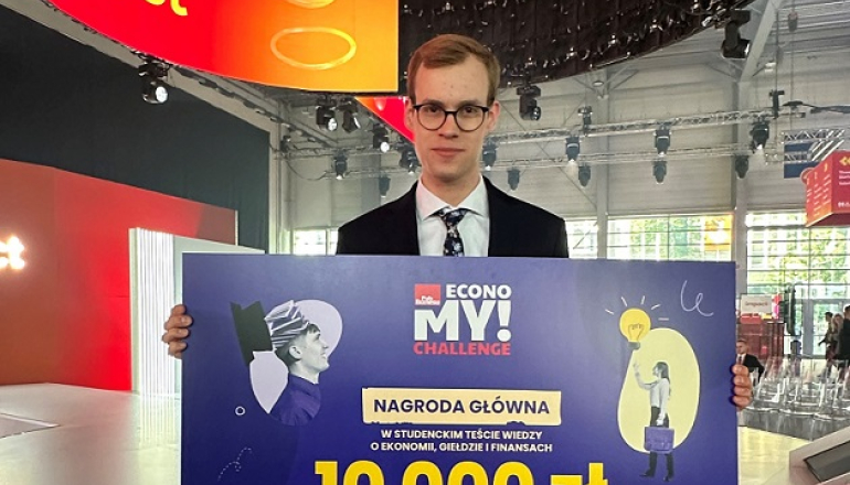 młody mężczyzna trzyma w ręku planszę informującą, że wygrał 10 000 zł w konkursie 