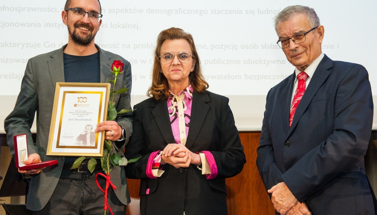 na zdjęciu stoją mężczyzna trzymający dyplom i na prawo od niego kobieta i mężczyzna