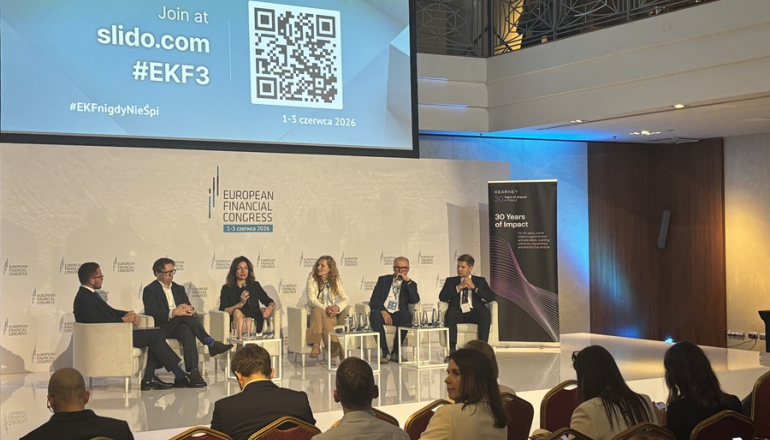 kilka osób dyskutuje na panelu, widać też ludzi siedzących na widowni