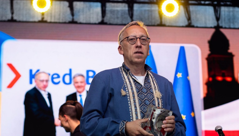mężczyzna w ludowej koszuli trzyma statuetkę na scenie