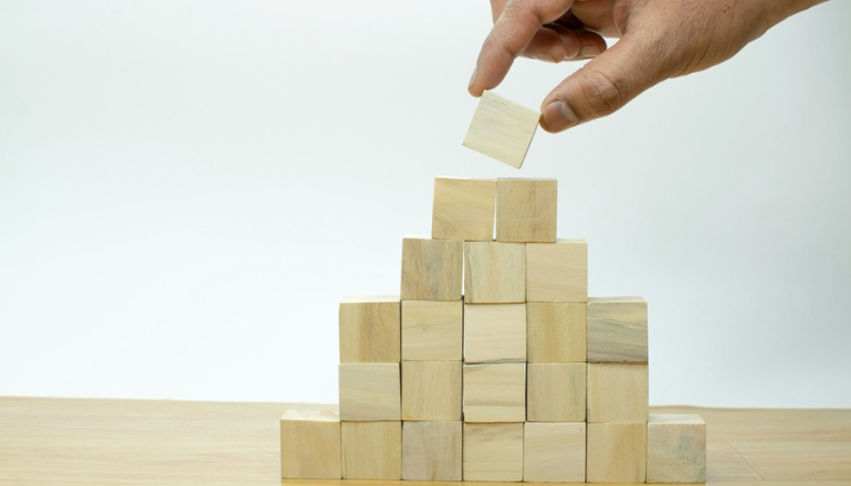 męska dłoń wyciąga jeden klocek z ułożonej piramidy 
