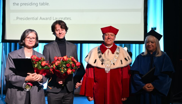 cztery osoby na zdjęciu, w tym laureat nagrody z bukietem kwiatów oraz rektor i prorektor uczelni