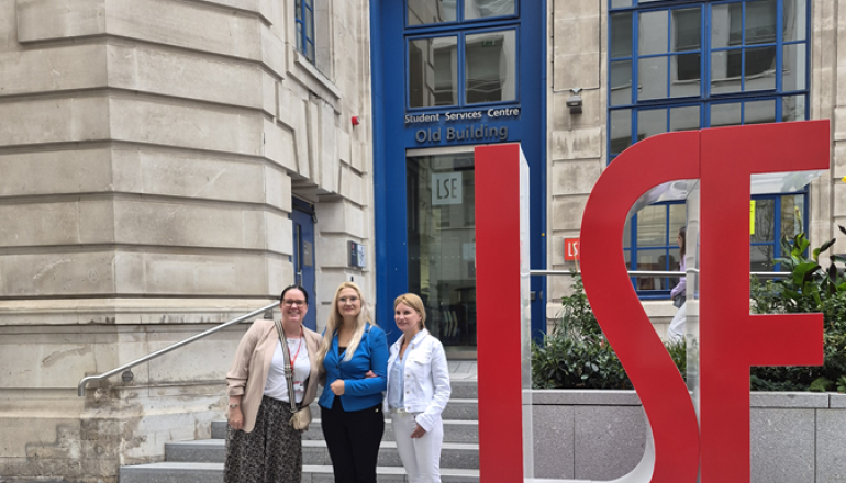 zdjęcie trzech kobiet przed siedzibą London School of Economics, kobiety stoją przy dużym akronimie LSE 