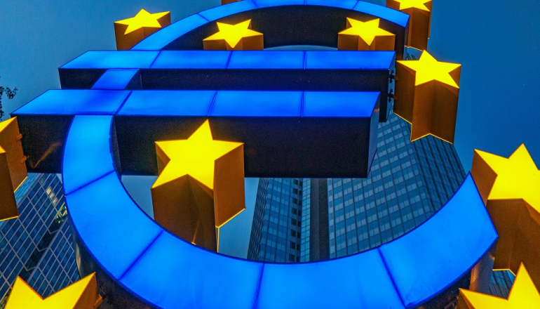 niebieski znak euro i żółte gwiazdki na tle wieżowców