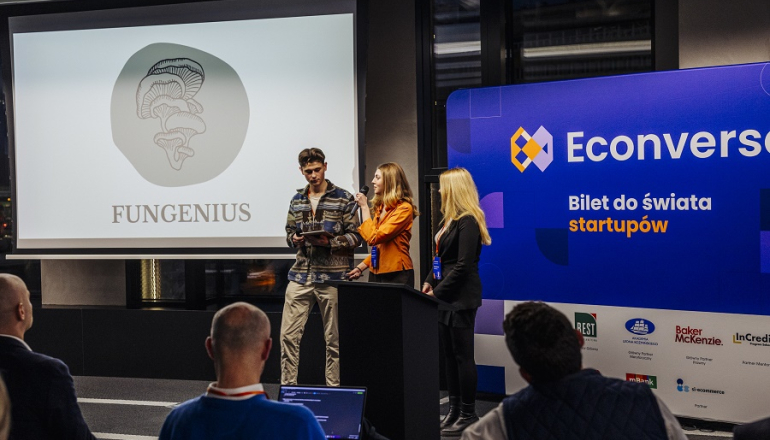dwie młode kobiety i mężczyzna prezentują na scenie swój projekt startupu