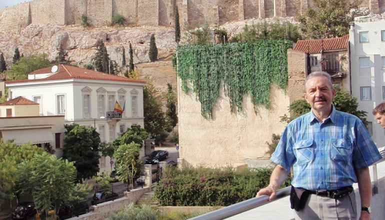 mężczyzna stoi przy murze; w tle grecki Akropol