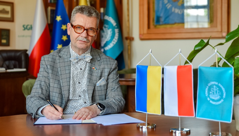 mężczyzna podpisuje dokumenty, obok proporczyki z flagą Ukrainy, Polski i SGH