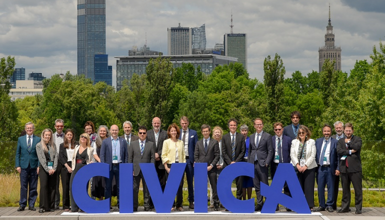 grupa osób na tle panoramy Warszawy, z przodu niebieski napis CIVICA