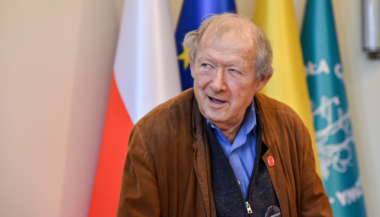 mężczyzna na tle flagi polskiej, unijnej, Warszawy i SGH