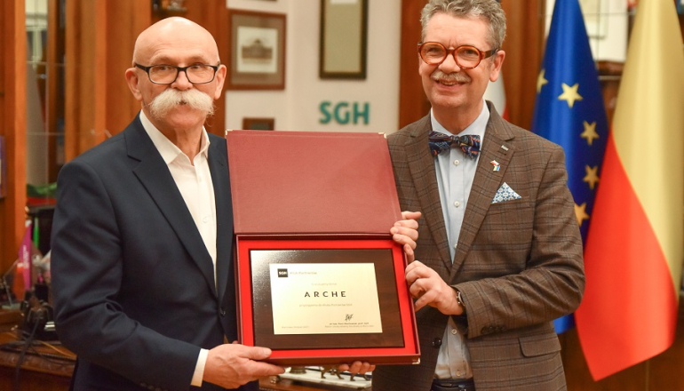 dwóch mężczyzn trzyma w rękach mosiężną tabliczkę informującą o przyjęciu firmy Arche do Klubu Partnerów SGH