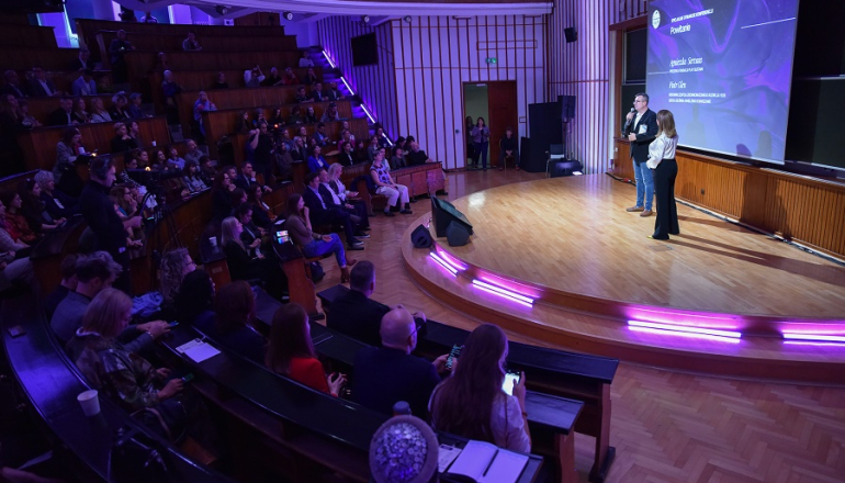 uczelniana aula wypełniona słuchaczami podczas konferencji; na scenie kobieta i mężczyzna