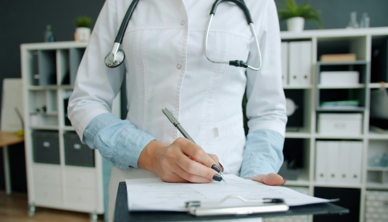 postać kobiety w fartuchu lekarskim i ze stetoskopem na szyi notuje coś na kartce