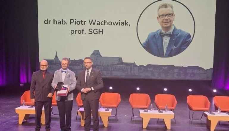 trzech mężczyzn stoi na scenie, jeden odbiera nagrodę