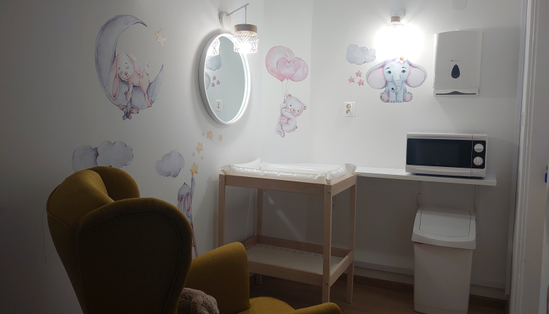 zdjęcie pokoju dla matki z dzieckiem; widać fragment fotela, lustro, przewijak dla niemowląt, mikrofalówkę, kosz na śmieci; na ścianach naklejki dla dzieci: misie, baloniki