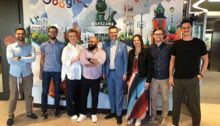 grupa osób stoi przed ścianą z napisem Google