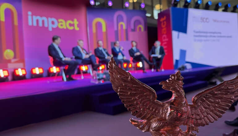 na pierwszym planie rzeźba godła dziennika "Rzeczpospolita" w tle paneliści rozmawiają na kongresie
