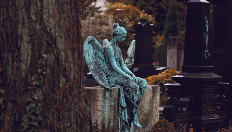 Zdjęcie kolorowe. Rzeźba anioła na tle cmentarza