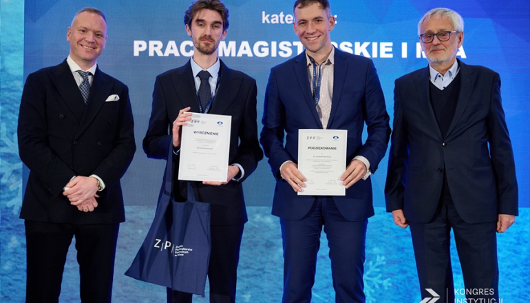 czterech mężczyzn na scenie; dwóch trzyma w rękach dyplomy z podziękowaniami