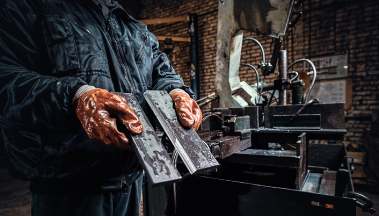 Na zdjęciu pracownik w rękawicach ochronnych trzyma świeżo ścięty kawałek metalu - autor fxquadro