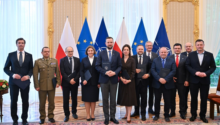 grono oficjeli pozuje do zdjęcia; w tle flagi Polski, UE, NATO