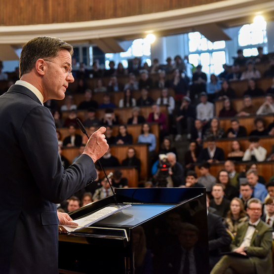 mężczyzna za mównicą przemawiający do pełnej ludzi auli
