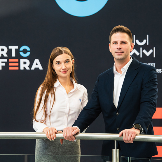 Kobieta i mężczyzna przy barierce na tle banera z napisem Kortosfera