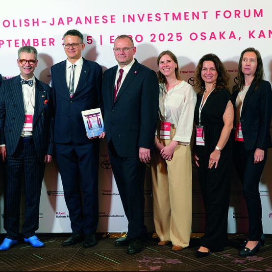 Dziewięć osób w oficjalnych strojach na tle baneru polsko-japońskiego forum inwestycyjnego