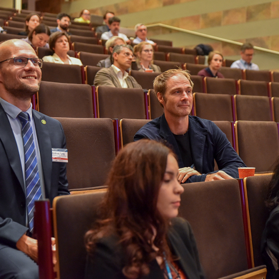 ludzie siedzący w ławkach w auli I budynku C