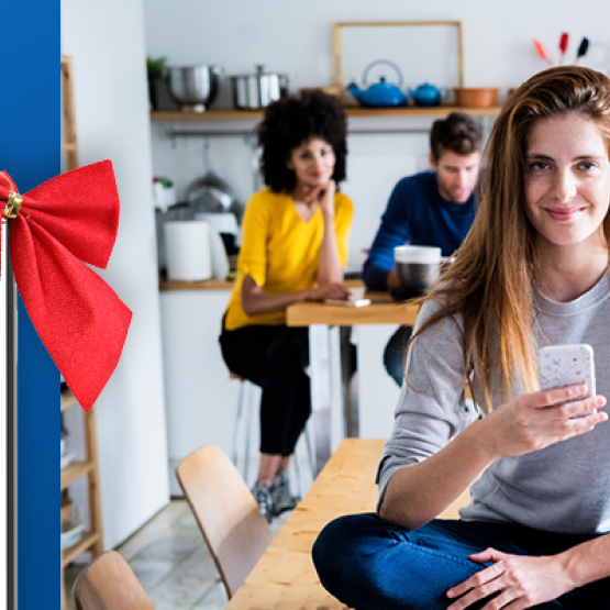 na pierwszym planie kobieta trzymająca komórkę, obok telefon komórkowy z czerwona kokardą