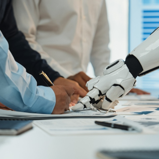 dwie osoby (widać tylko tułowie) dyskutują nad jakimś planem na biurku, pokazując w jedno miejsce palcami; z prawej strony widać także rękę robota