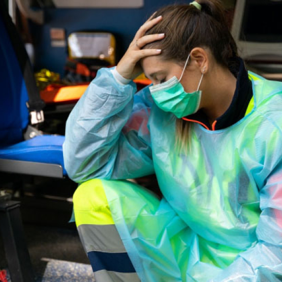 ratowniczka medyczna siedzi przy wyjściu do karetki, trzyma się za głowę w geście zmęczenia